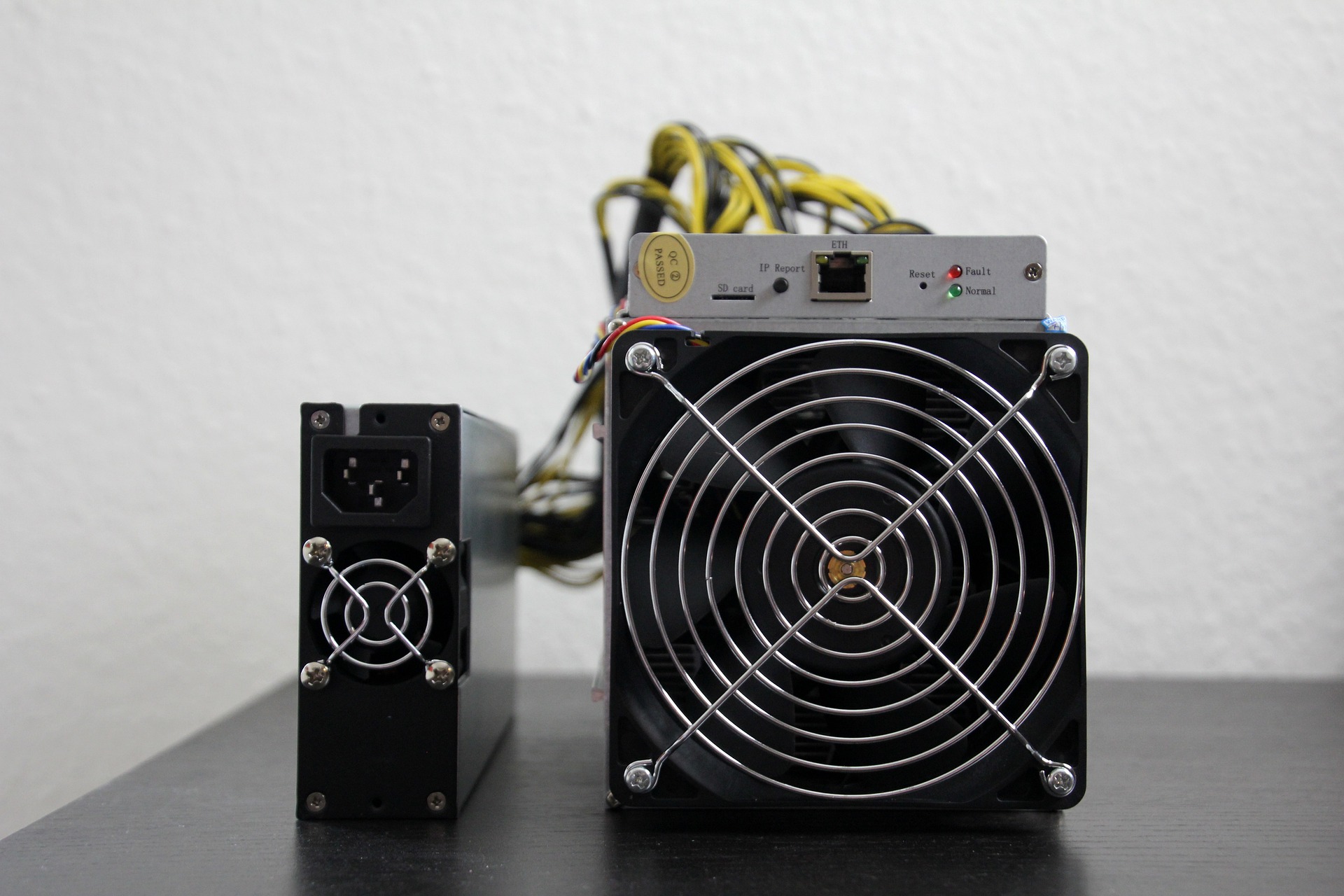 ASIC miner sitting on black table against a white wall.