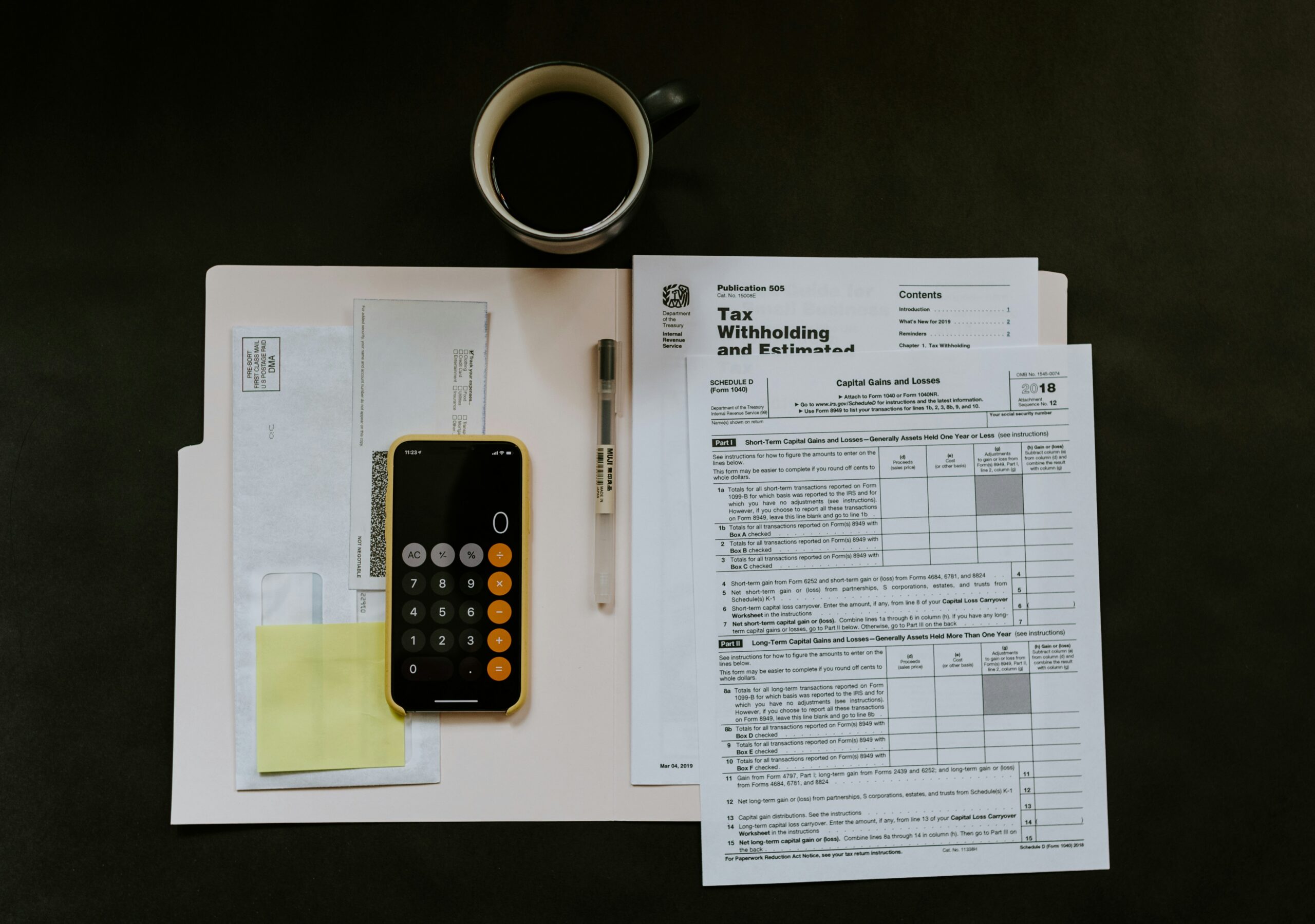 iPhone calculator, mug of coffee and tax documents laid on desk.