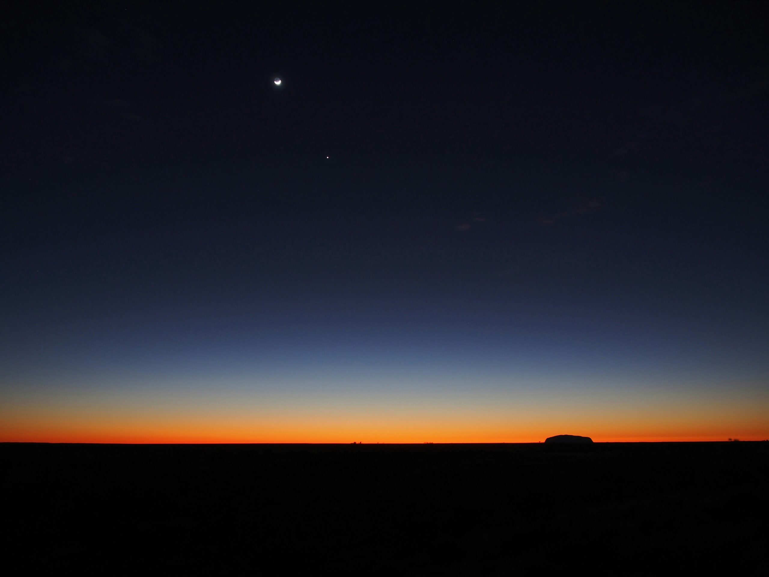 Horizon at night in Uluru, Australia, with moon and stars visible.