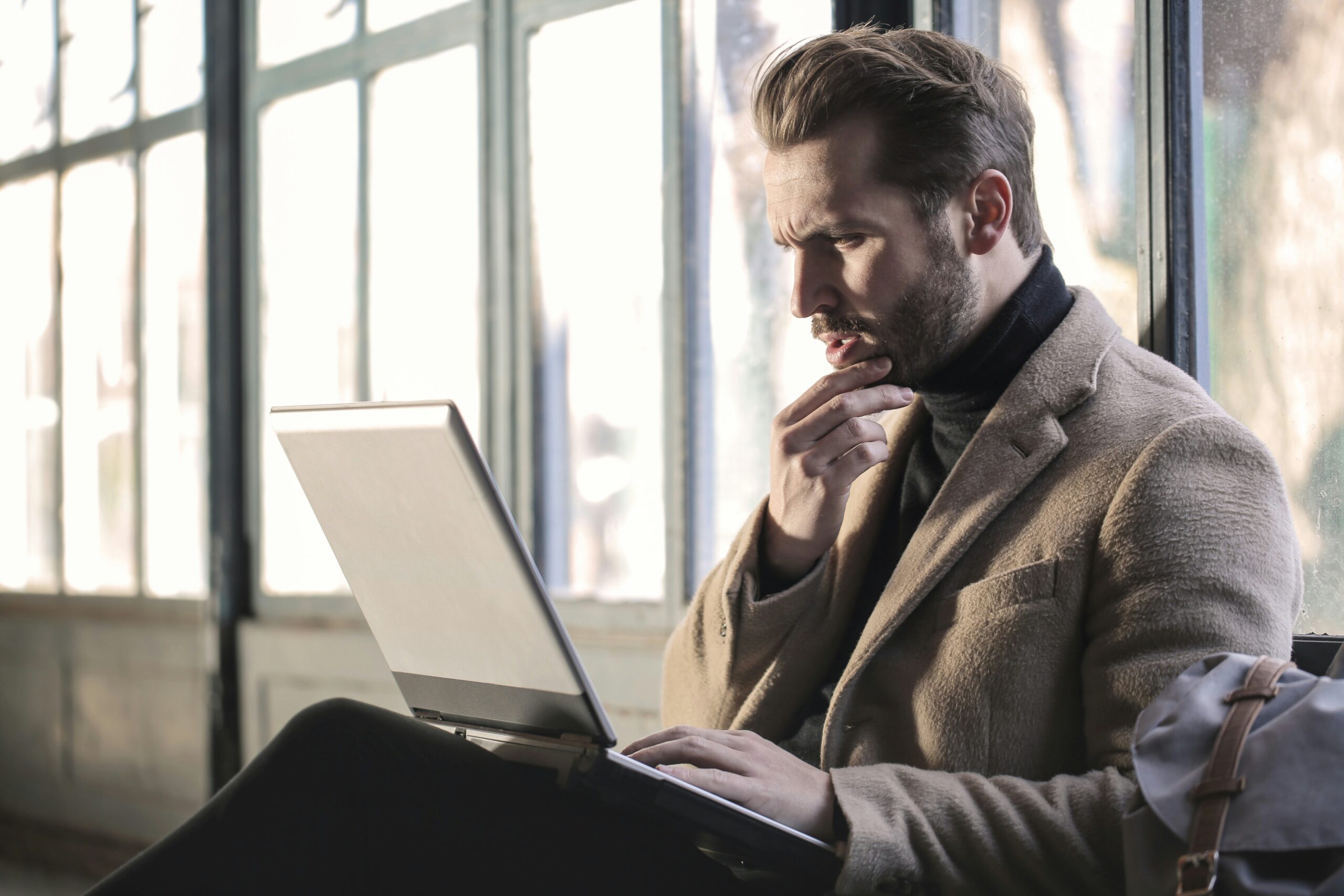 Person dressed smartly looking at laptop screen thinking.