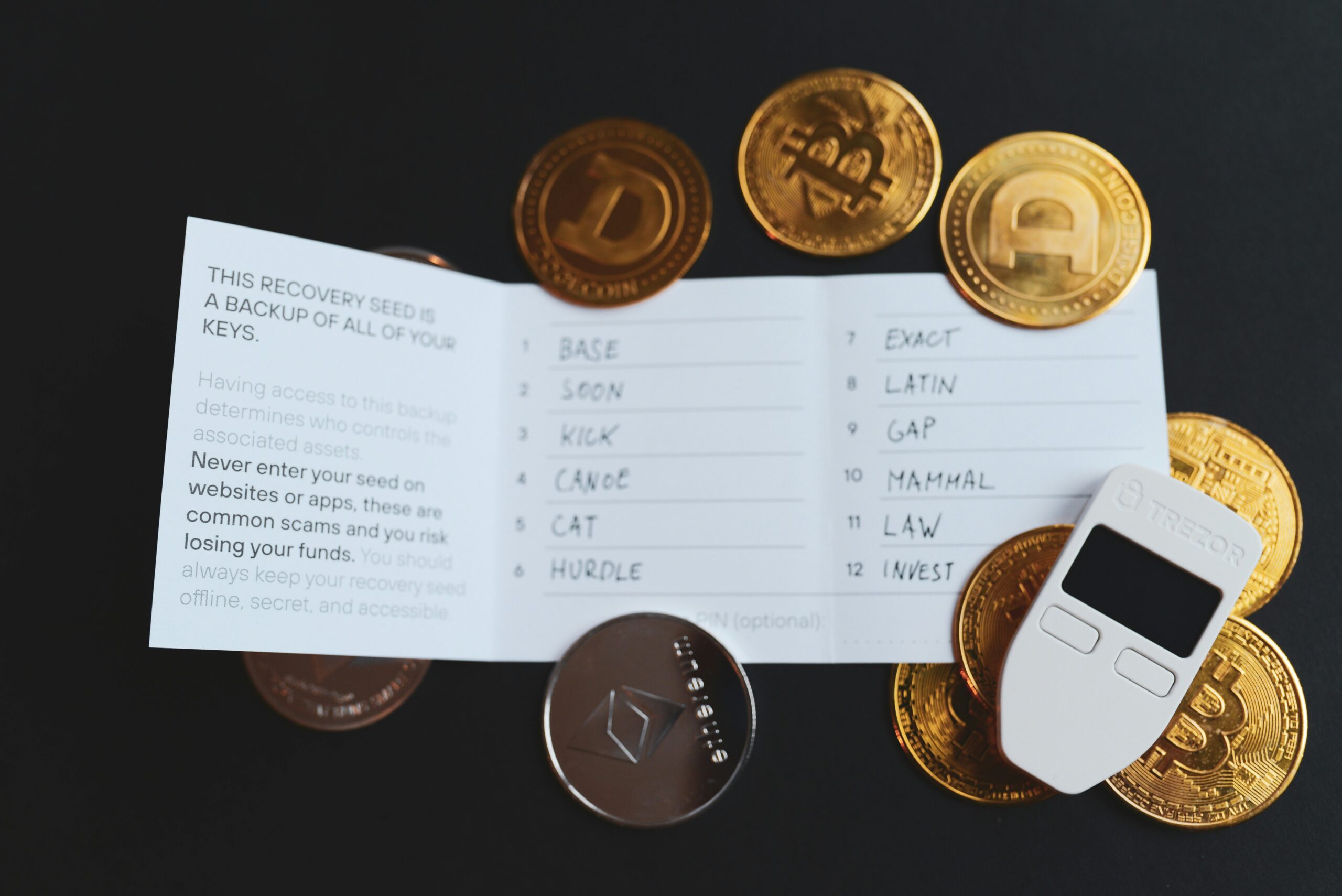 Seed phrase written on card next to a Trezor hardware wallet and golden bitcoins.